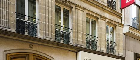 A building facade with ornate balconies, a prominent red sign, and a storefront labeled "OPTIQUE."