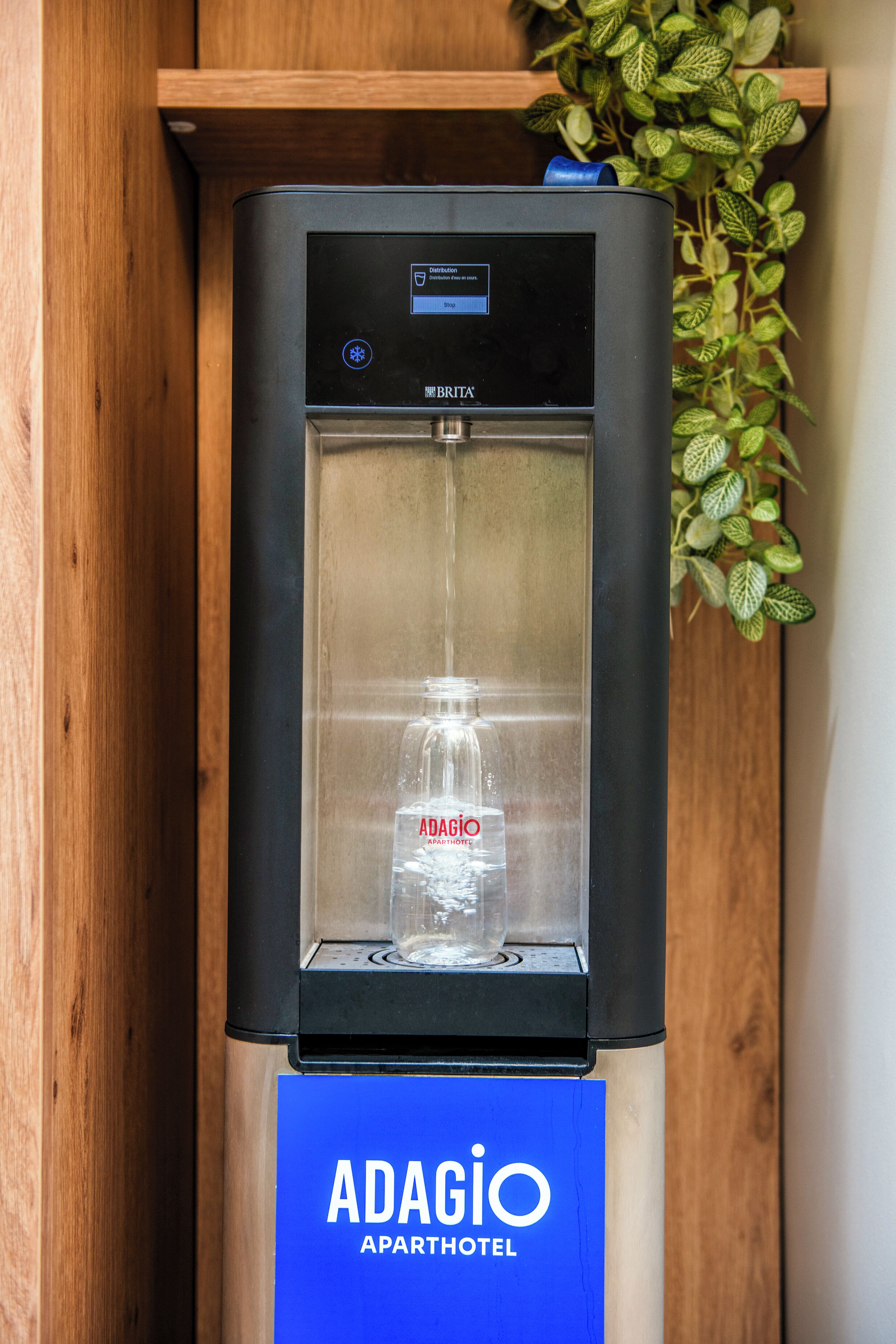 Un dispensador de agua con una botella de vidrio transparente en su interior, con la etiqueta "ADAGIO APARTHOTEL".