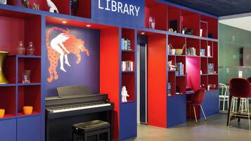 Une bibliothèque avec des étagères rouges et bleues, un piano et une fresque représentant une carte du monde.