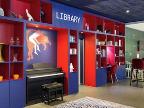 Una biblioteca con estanterías rojas y azules, un piano y un mural de un mapa mundial.