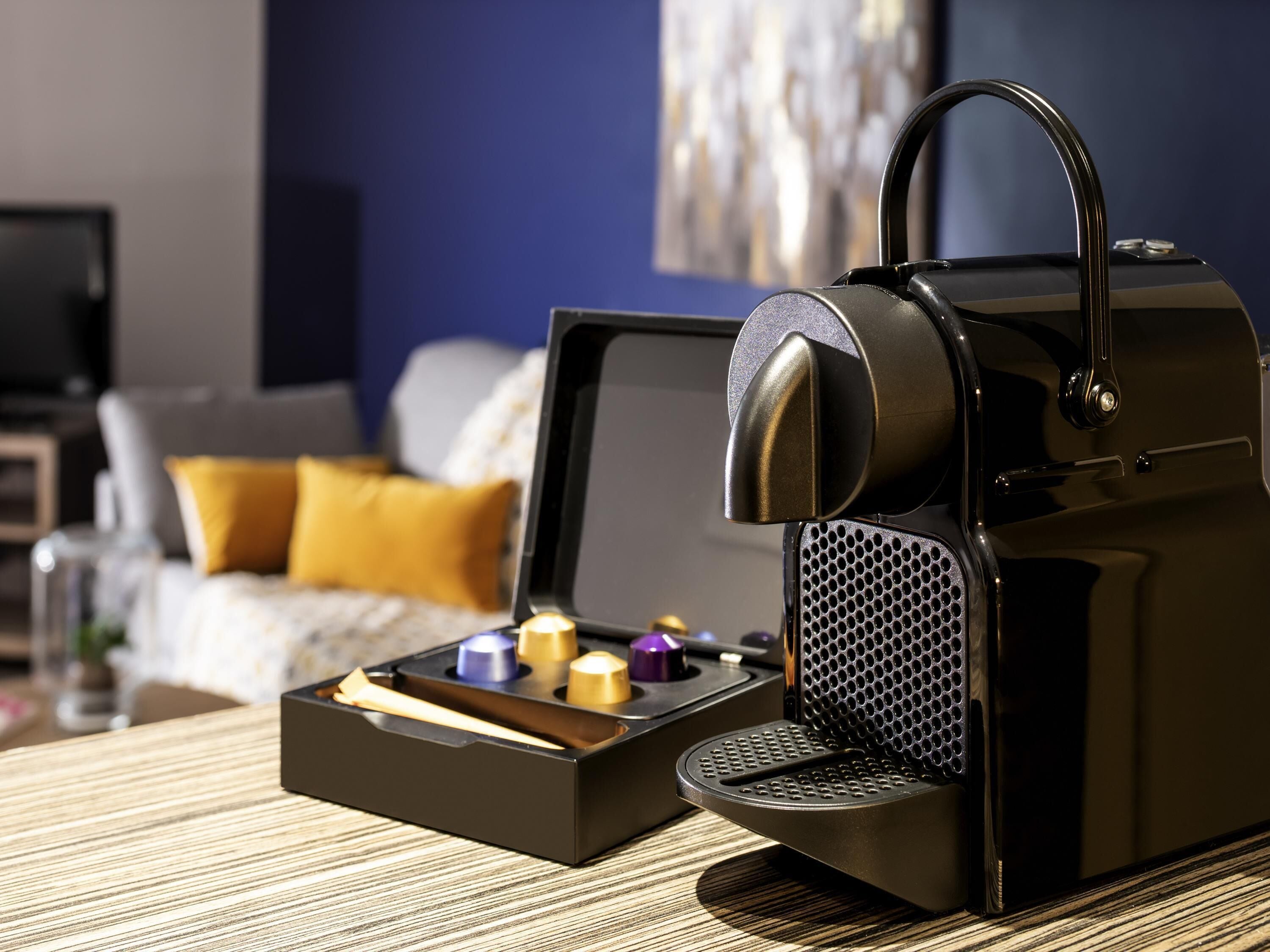 Een moderne keuken met een koffieapparaat, een houten tafel en een bankstel op de achtergrond.