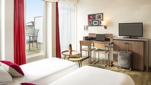 A hotel room with two beds, a desk with a computer, a television, and a suitcase. - Aparthotel Adagio Basel City (Basel)