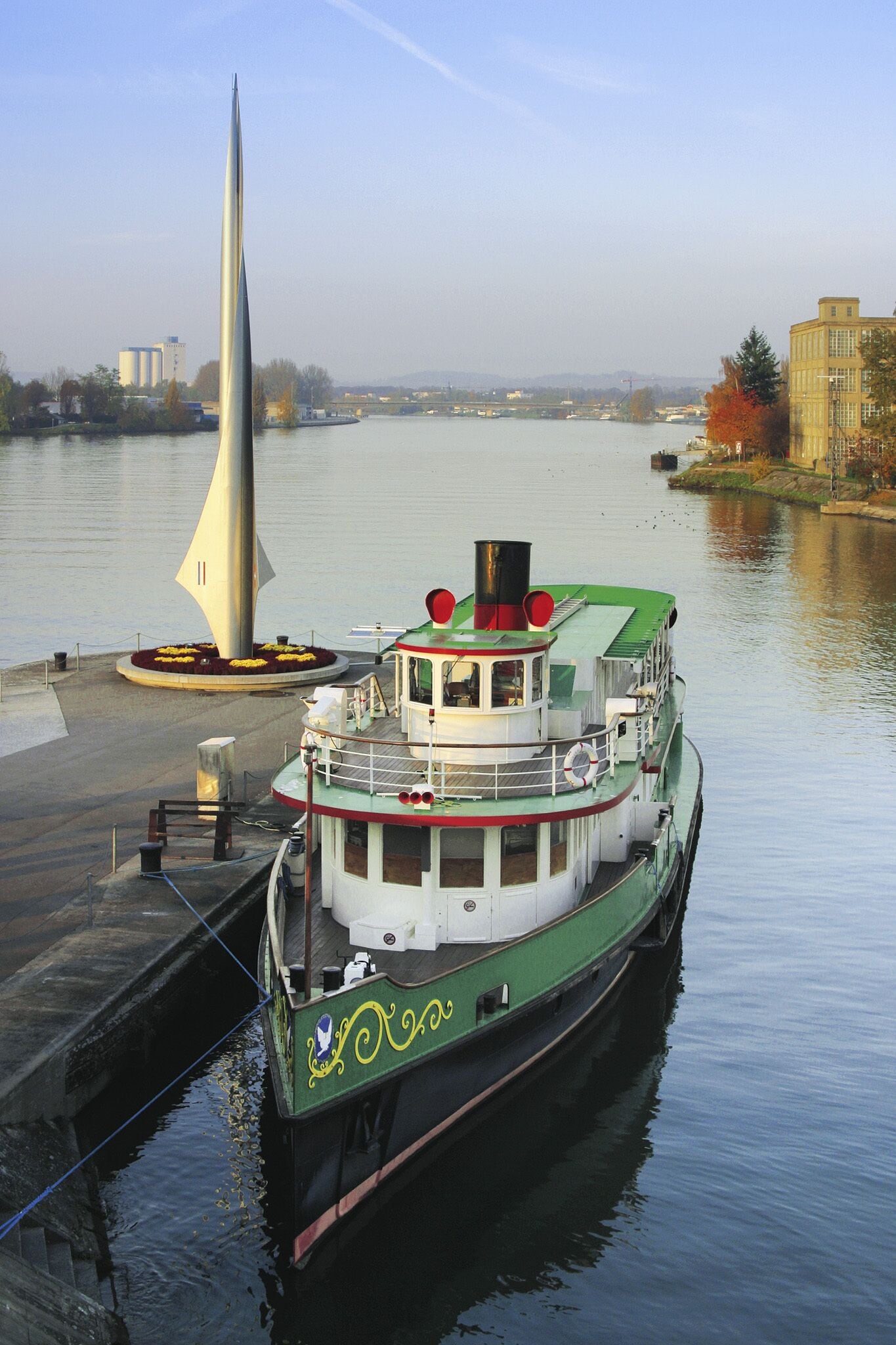 A green and white boat docked at a pier with a sail-like structure nearby.