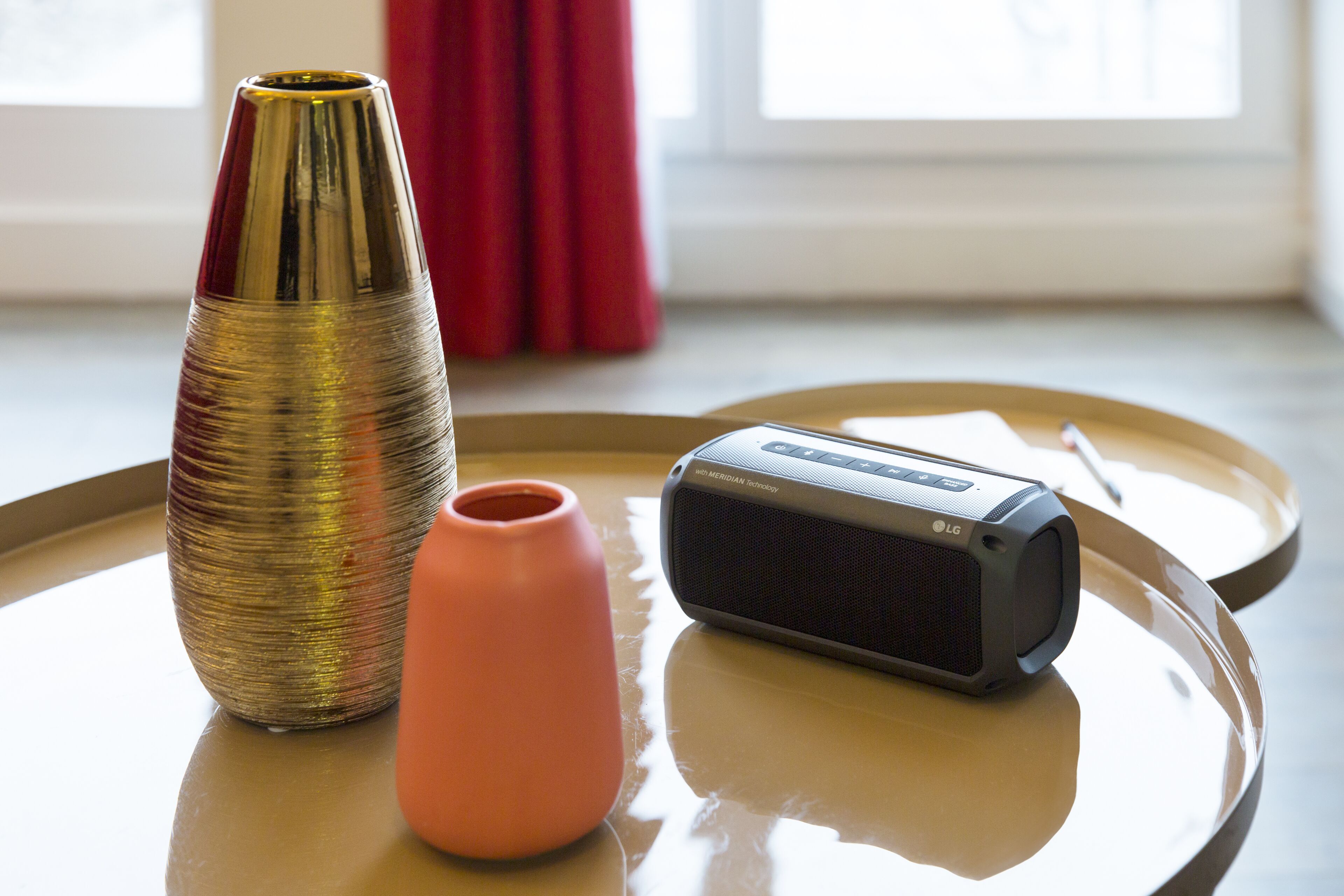 A table with a golden vase, a pink vase, and an LG speaker.