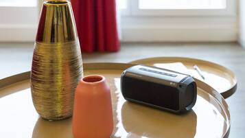 Una mesa con un jarrón dorado, un jarrón rosa y un altavoz LG.