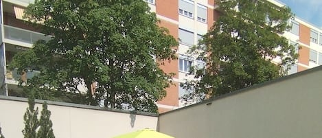 A garden pathway with a yellow umbrella, surrounded by greenery and flowers.