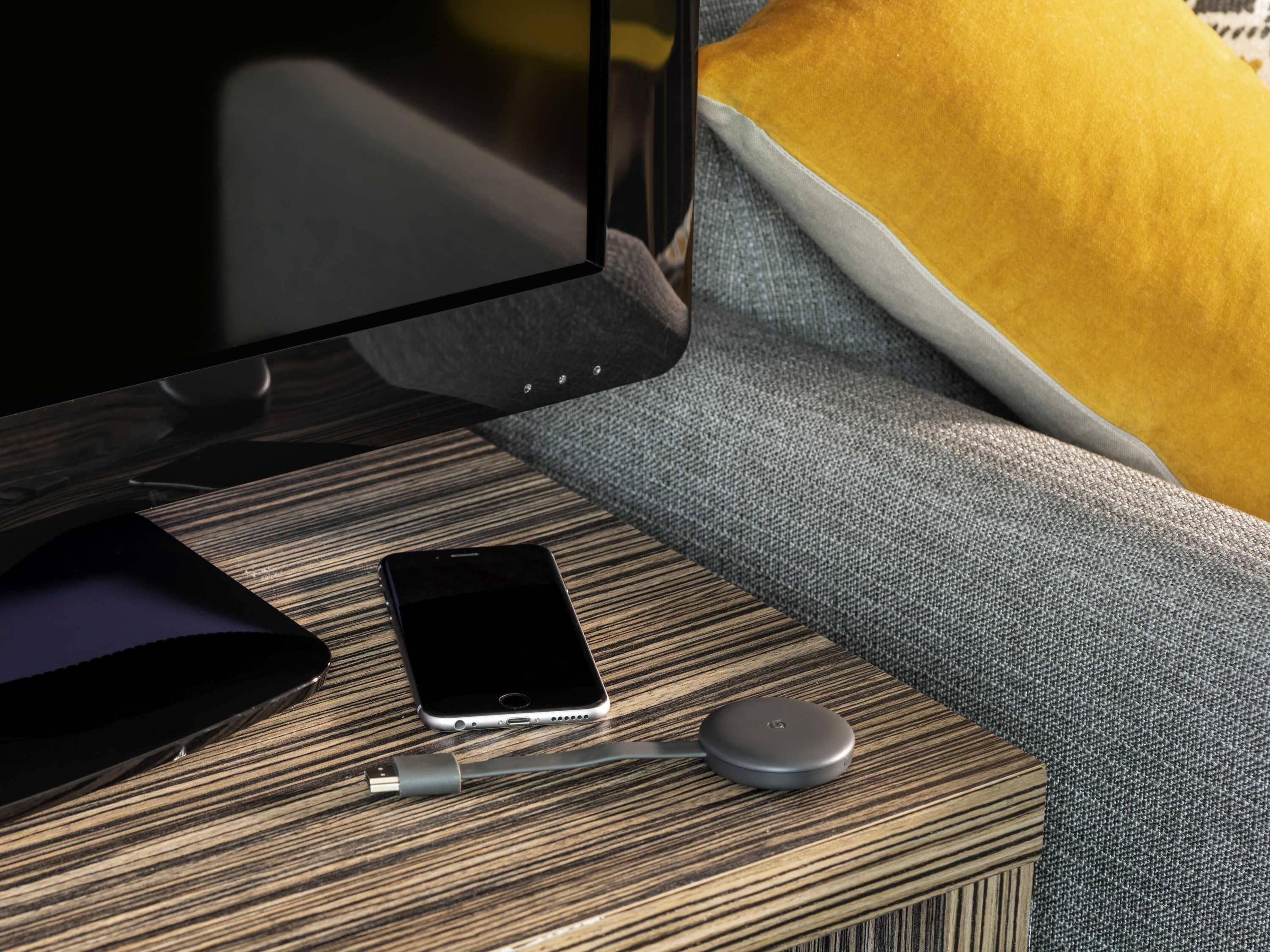 Una habitación moderna con una mesita de madera, un teléfono inteligente, un cargador con cable y un control remoto.