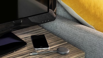 Una habitación moderna con una mesita de madera, un teléfono inteligente, un cargador con cable y un control remoto.