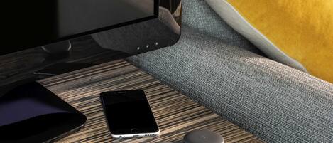 A modern room with a wooden side table, a smartphone, a wired charger, and a remote control.