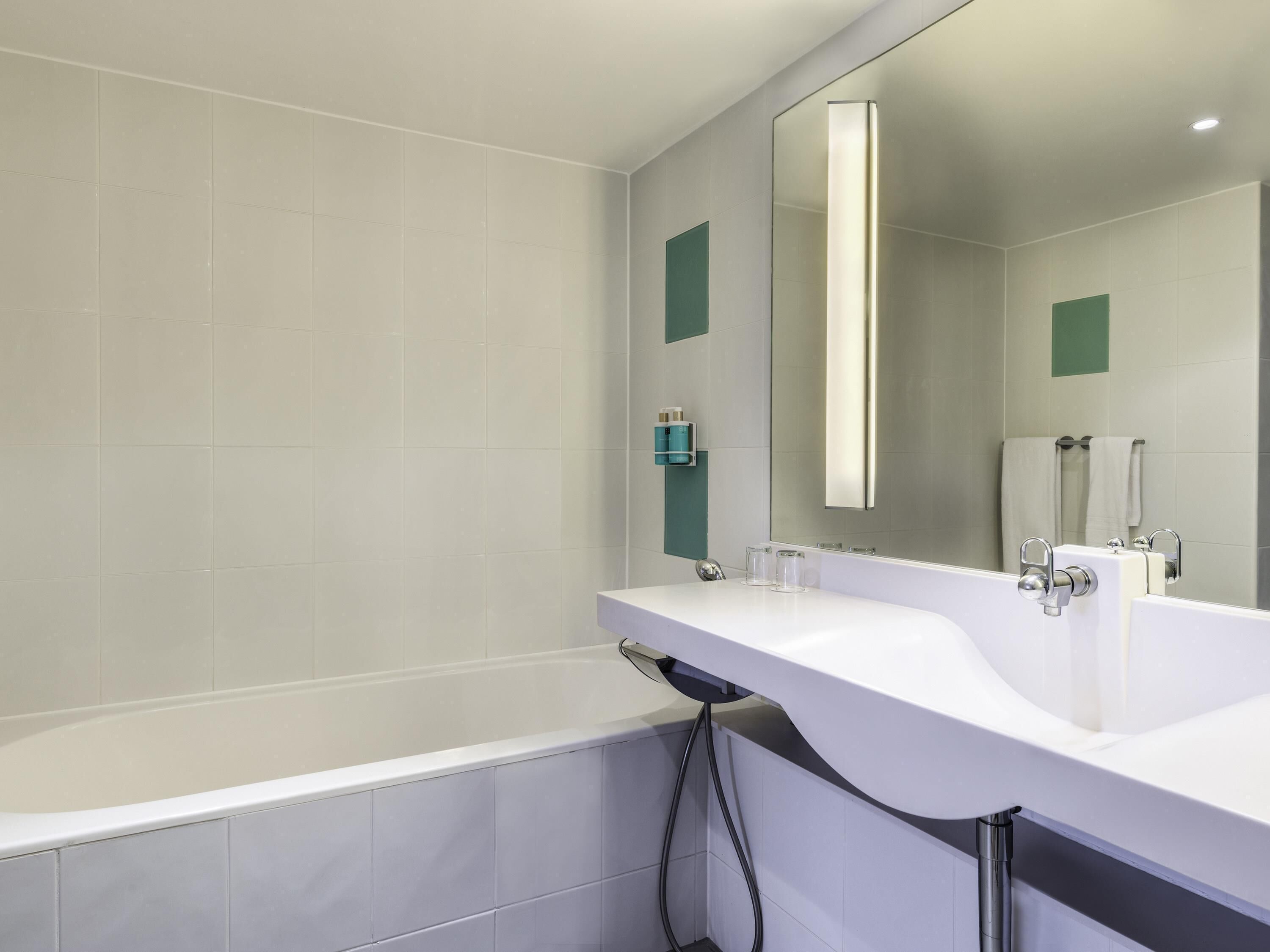 Un baño moderno con bañera, dos lavamanos, un espejo grande y un perchero para toallas.