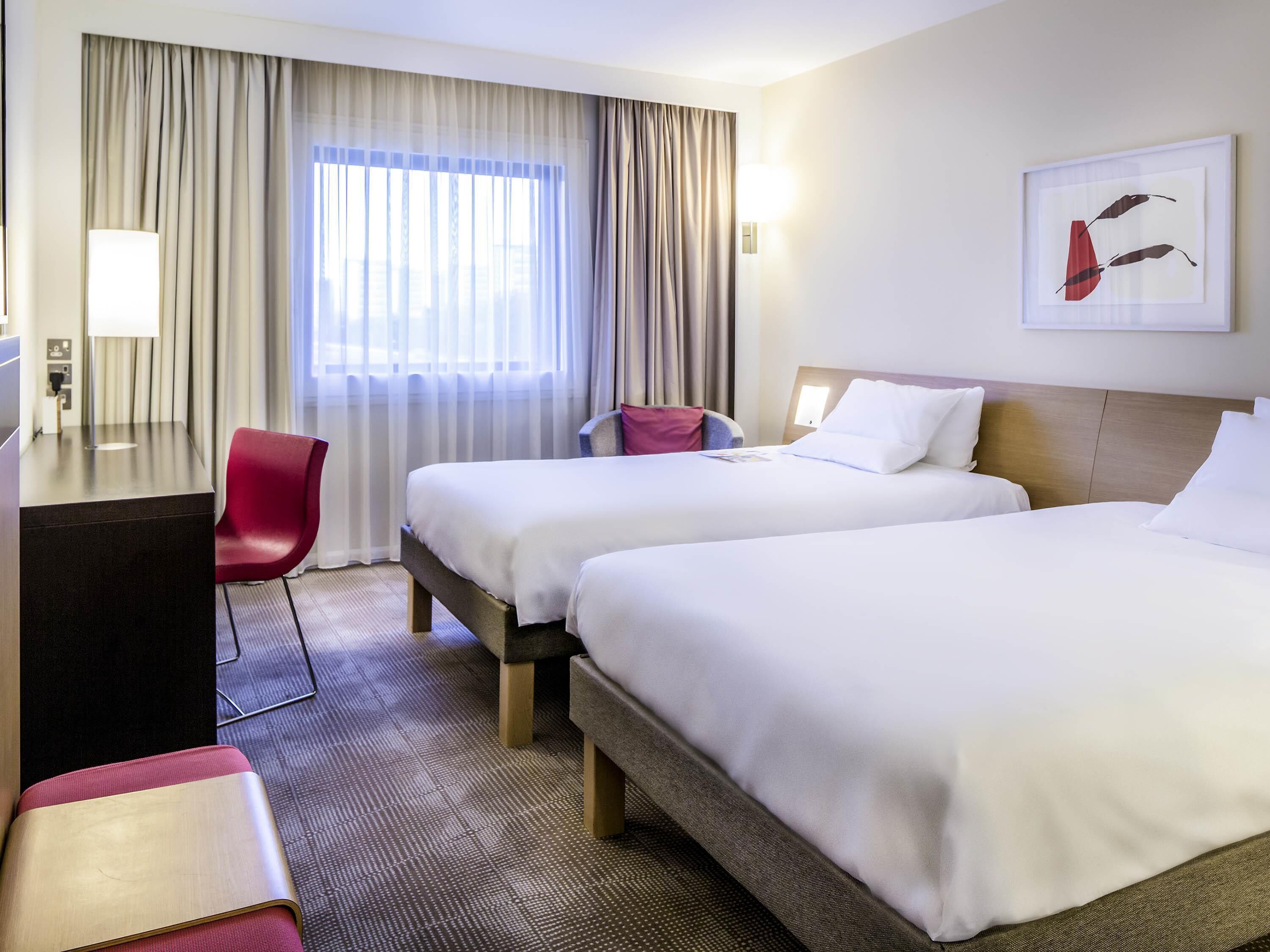 A hotel room with two beds, a desk, a chair, and a large window with curtains.