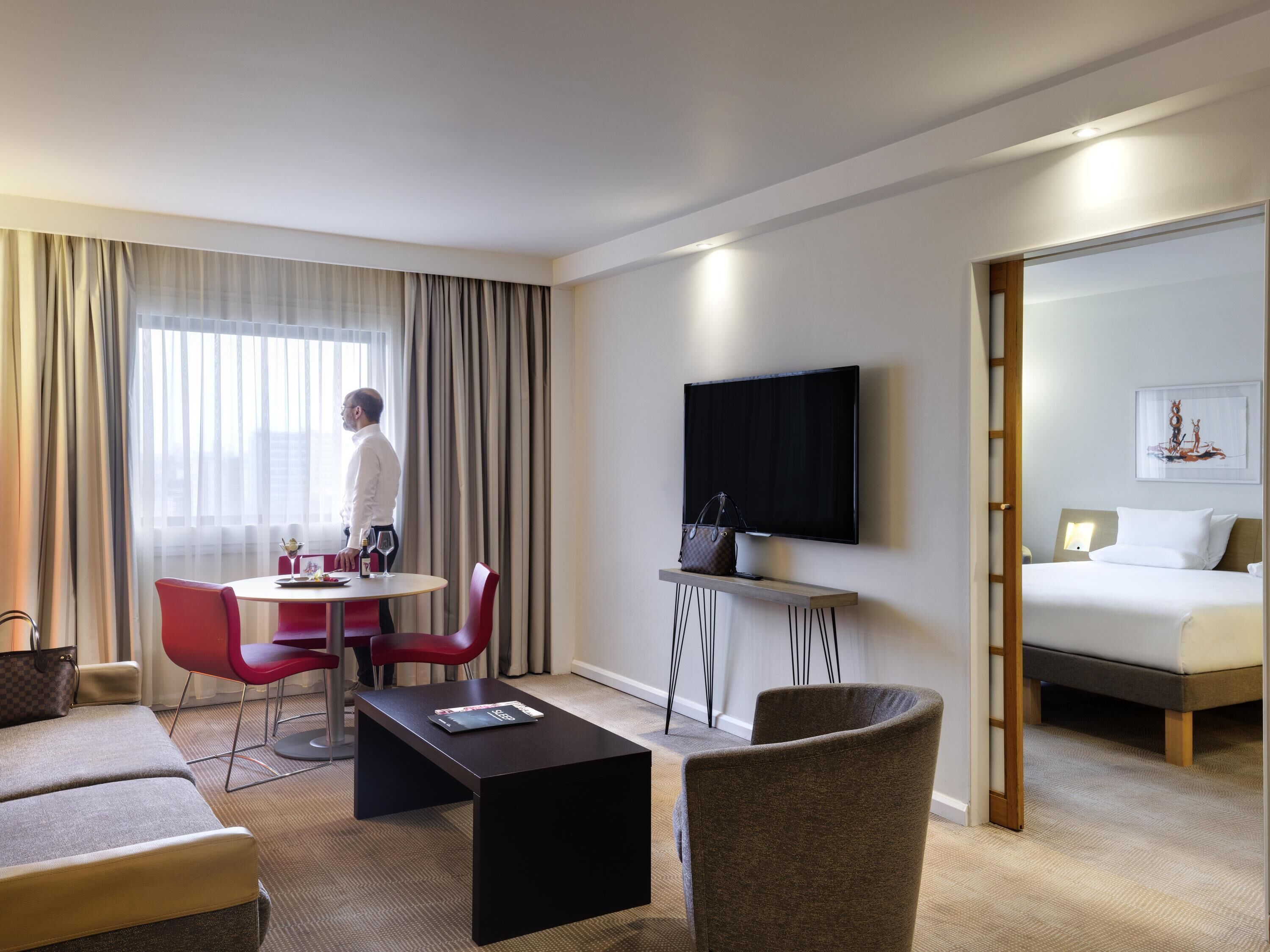 A hotel room with a bed, a TV, a dining area with a table and chairs, and a sofa.