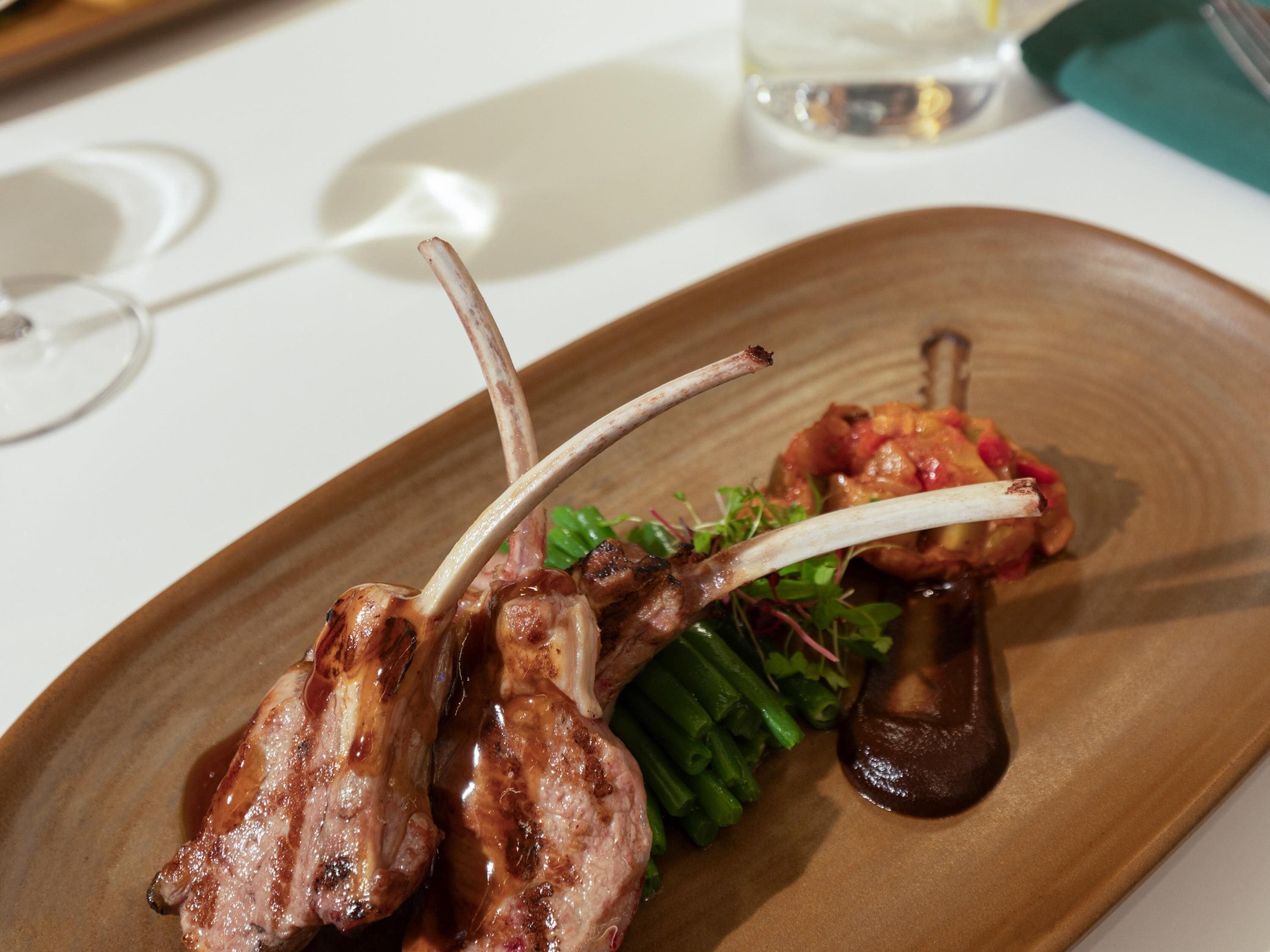 A plate with grilled lamb chops, greens, and a mushroom.