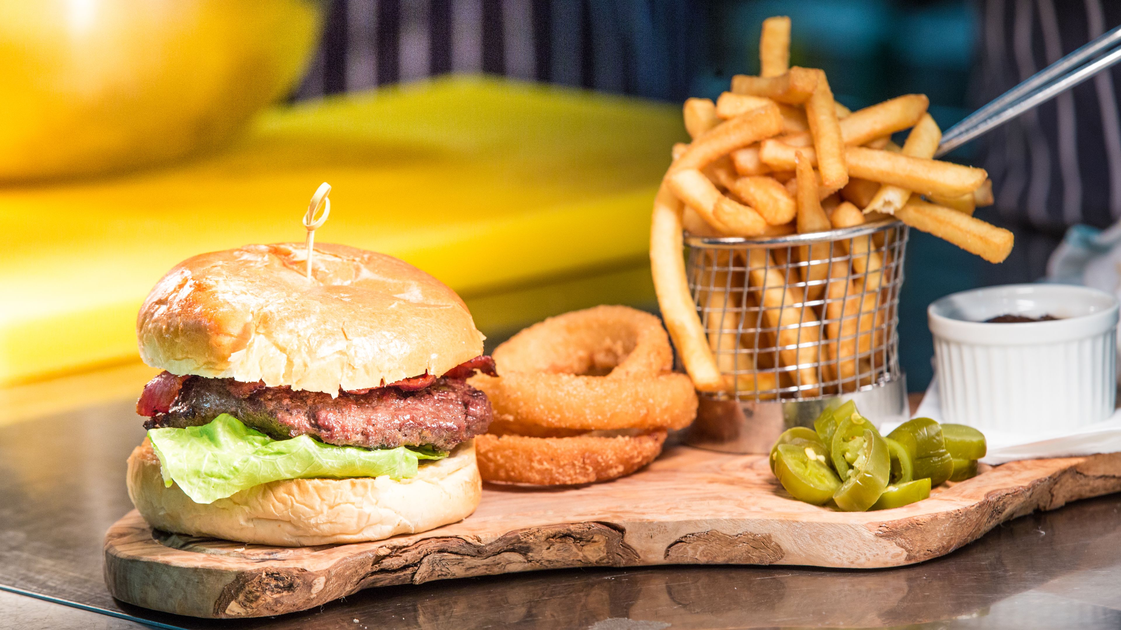 A meal with a burger, fries, onion rings, and pickles on a wooden board.