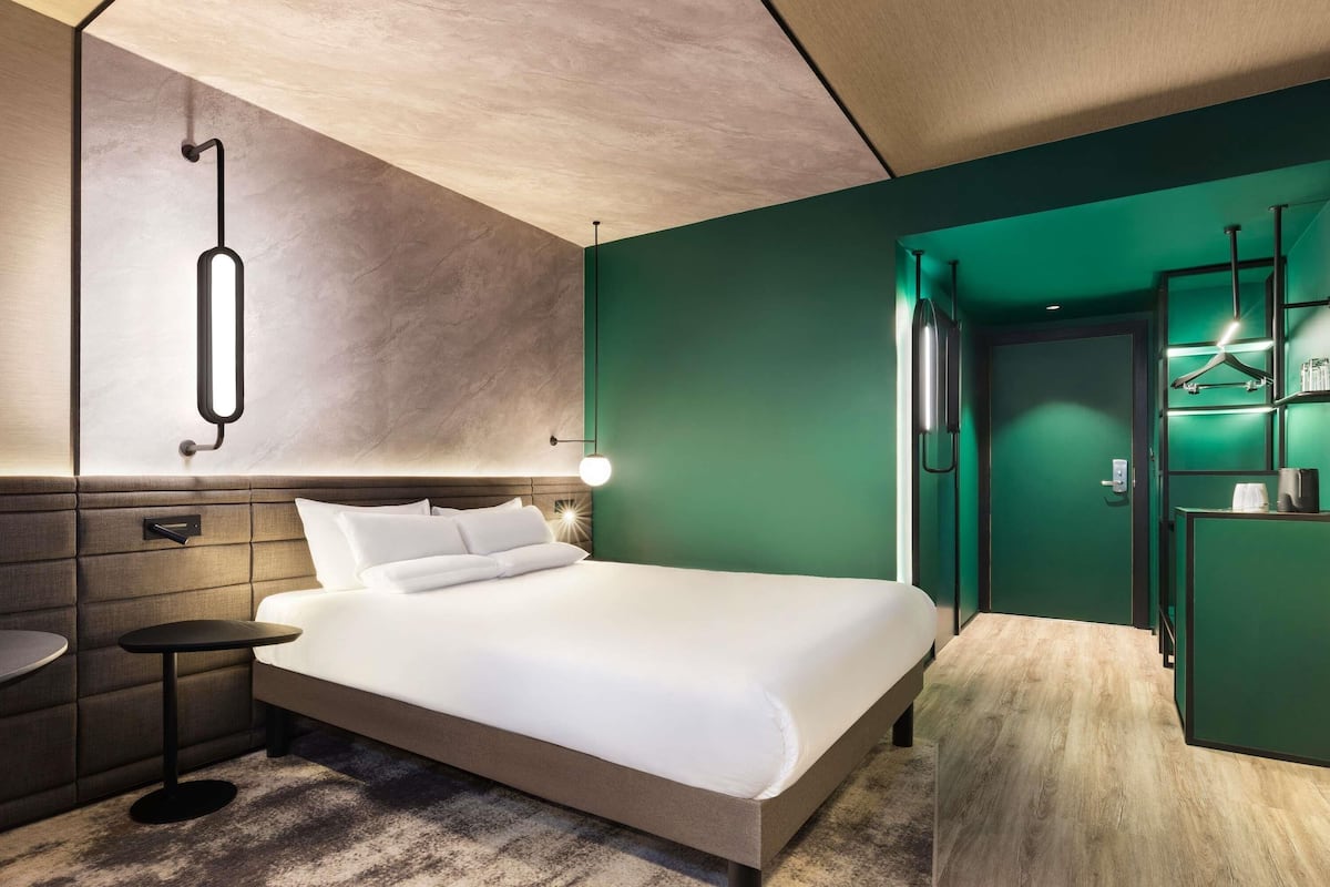 A modern hotel room with a bed, bedside table, and a green wall.