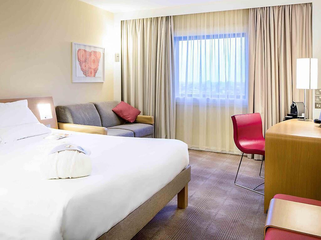 A hotel room with a bed, a sofa, a desk, a chair, and a window with curtains.