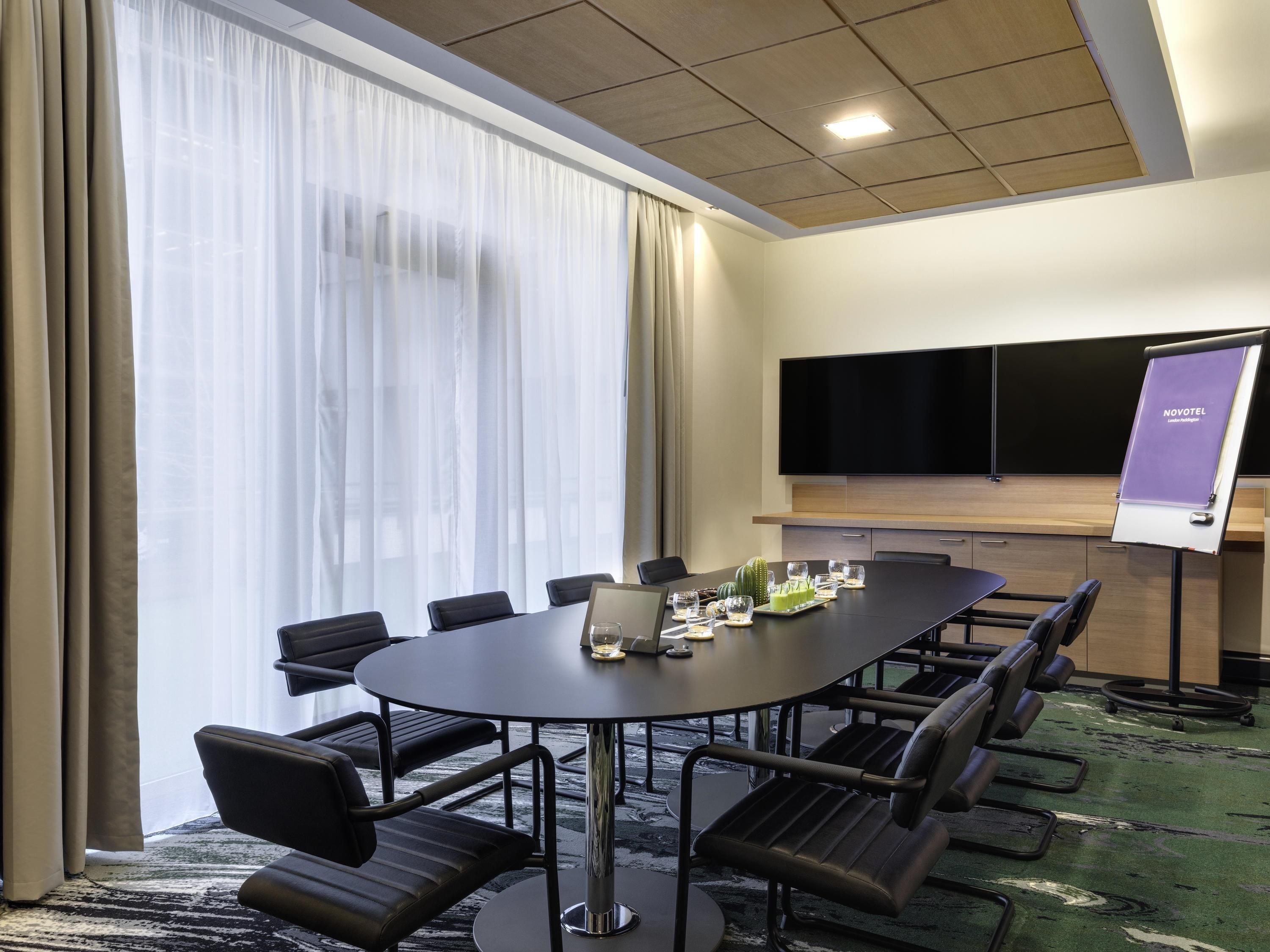 A conference room with a large table, chairs, a TV, and a presentation screen.