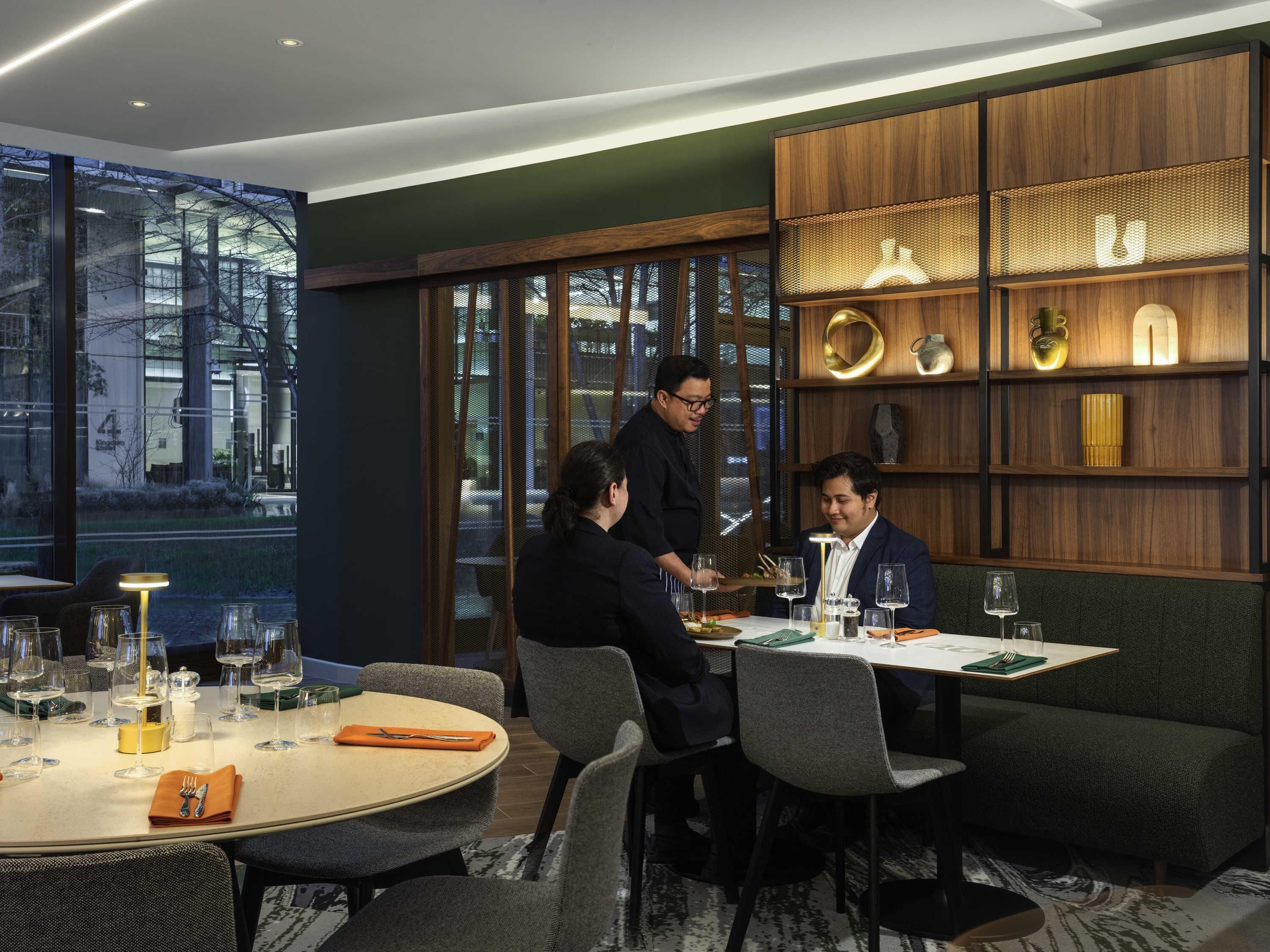 A modern dining area with a round table, chairs, and a waiter serving.