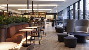 A modern interior with a bar area, seating, and large windows. - Novotel London Paddington (London)