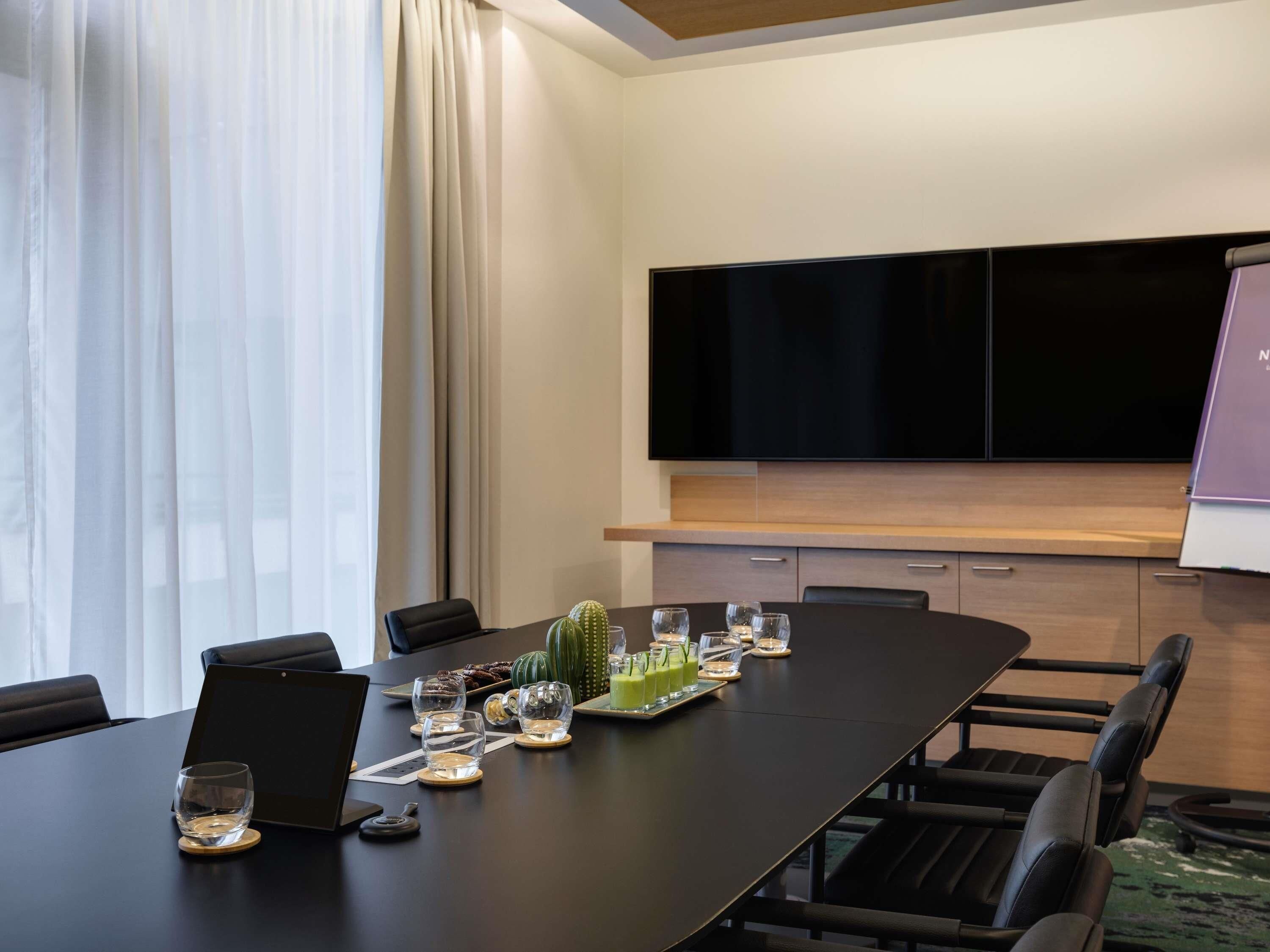 Una sala conferenze con un lungo tavolo, sedie, un portatile, un cactus e una televisione a schermo piatto.