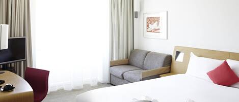 Una habitación de hotel con cama, escritorio, silla, televisor y cortinas.