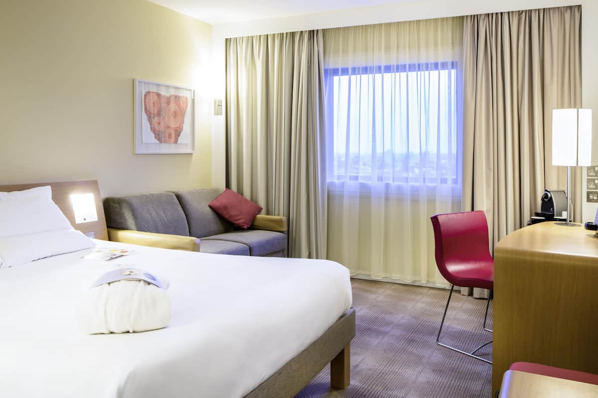 A hotel room with a large bed, a sofa, a desk, and a chair.