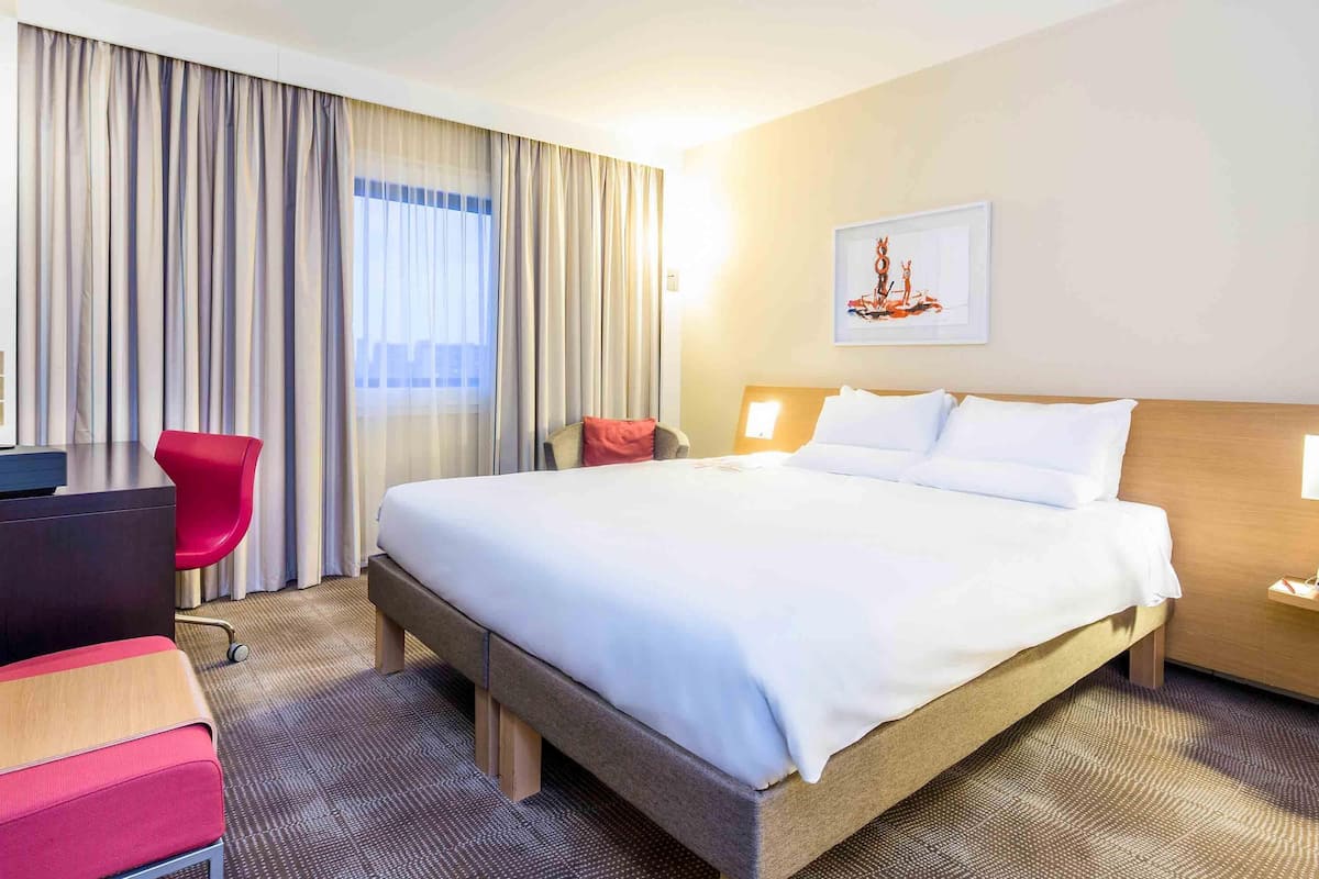 A hotel room with a large bed, a desk, a chair, and a window with curtains.