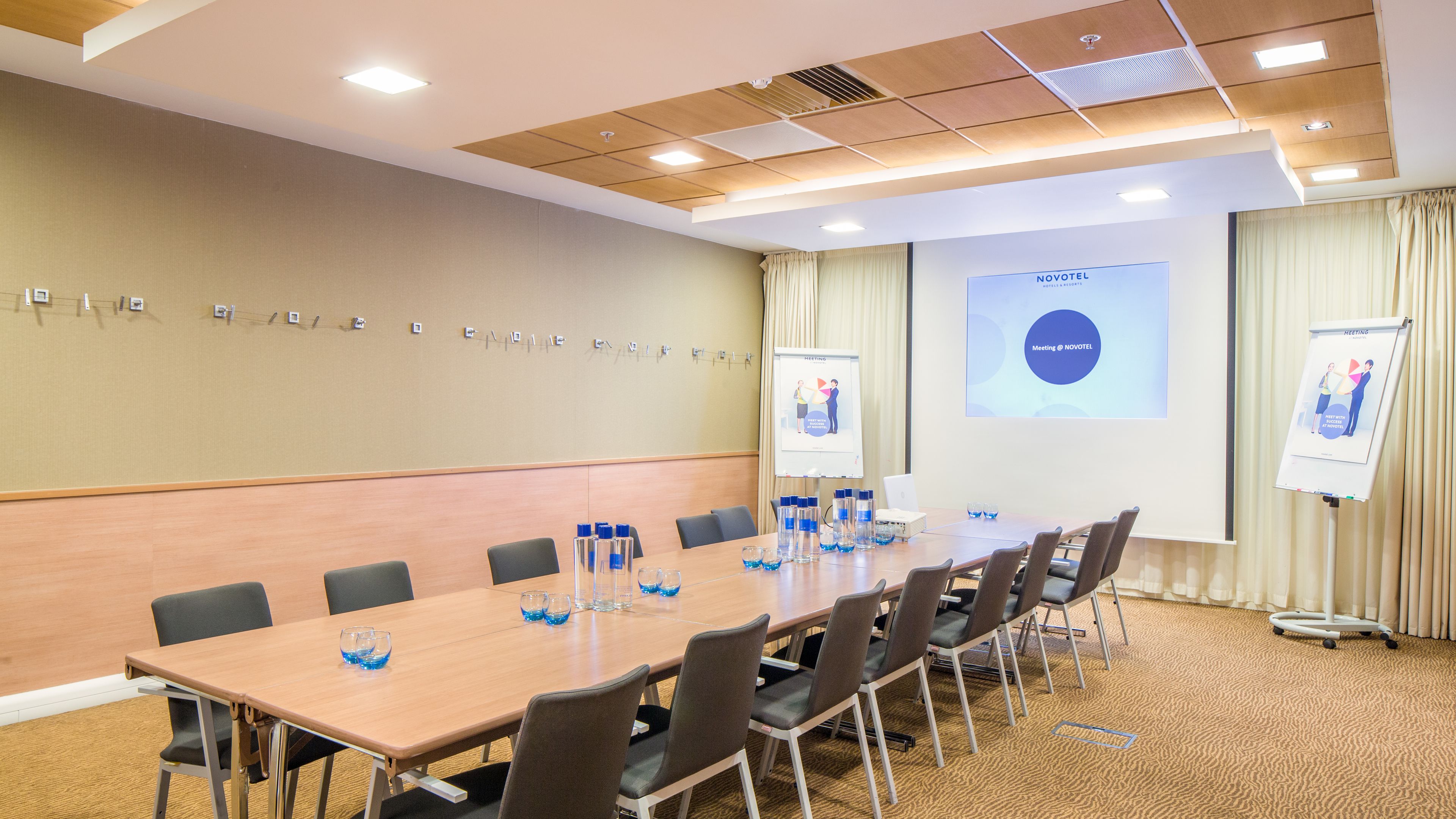A conference room with a long table, chairs, a projector screen, and a presentation board.
