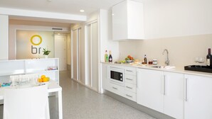 Cocina moderna con muebles blancos, horno integrado y encimera con botellas y frutas diversas.
