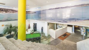 Un vestíbulo de hotel con mesa de billar, mostrador de recepción y un mural de paisaje costero.