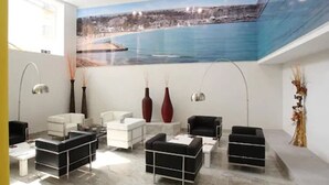 Un área de espera moderna con un amplio mural de una escena costera, mobiliario contemporáneo y jarrones decorativos.
