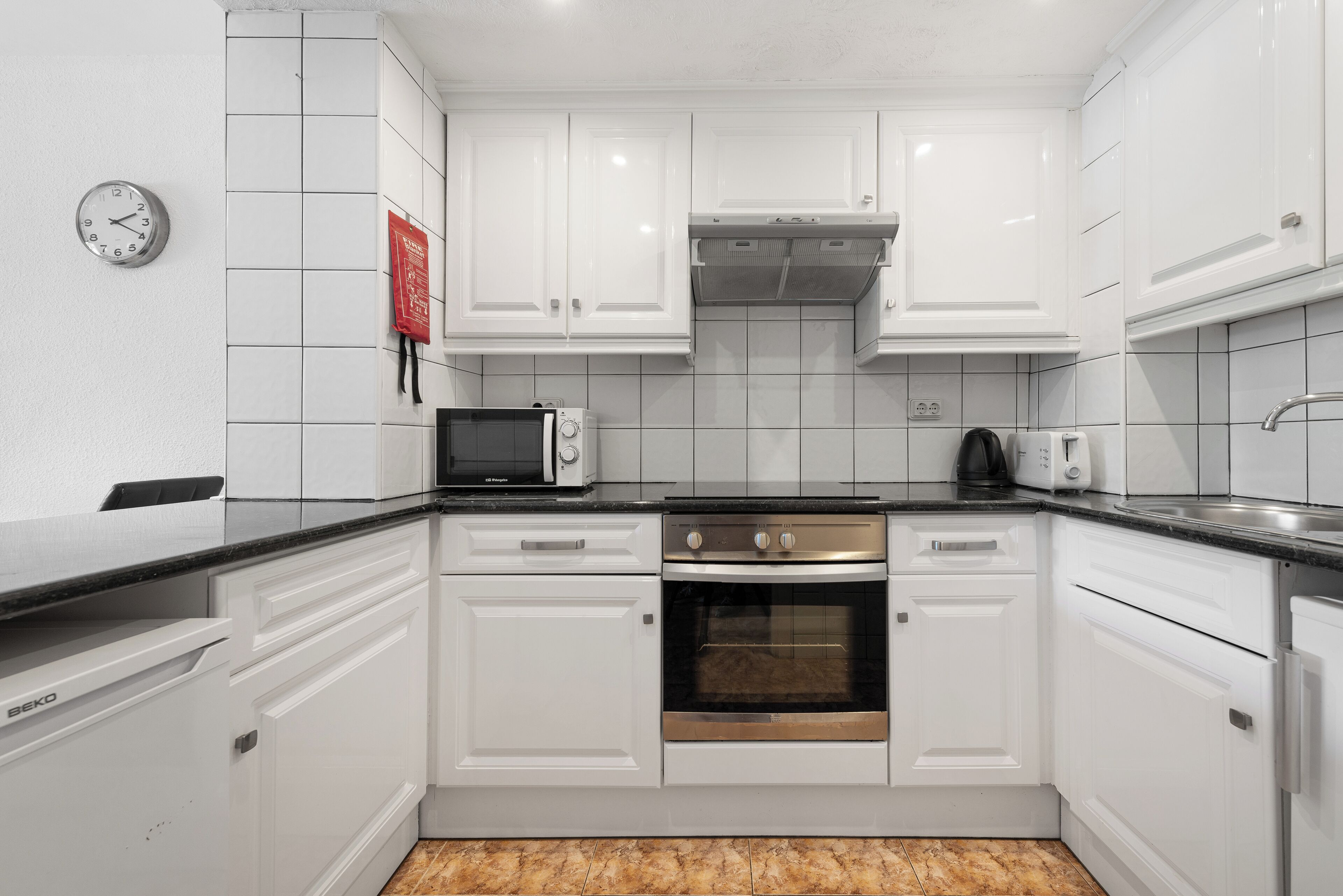 A modern kitchen with white cabinets, a microwave, an oven, and a clock on the wall.