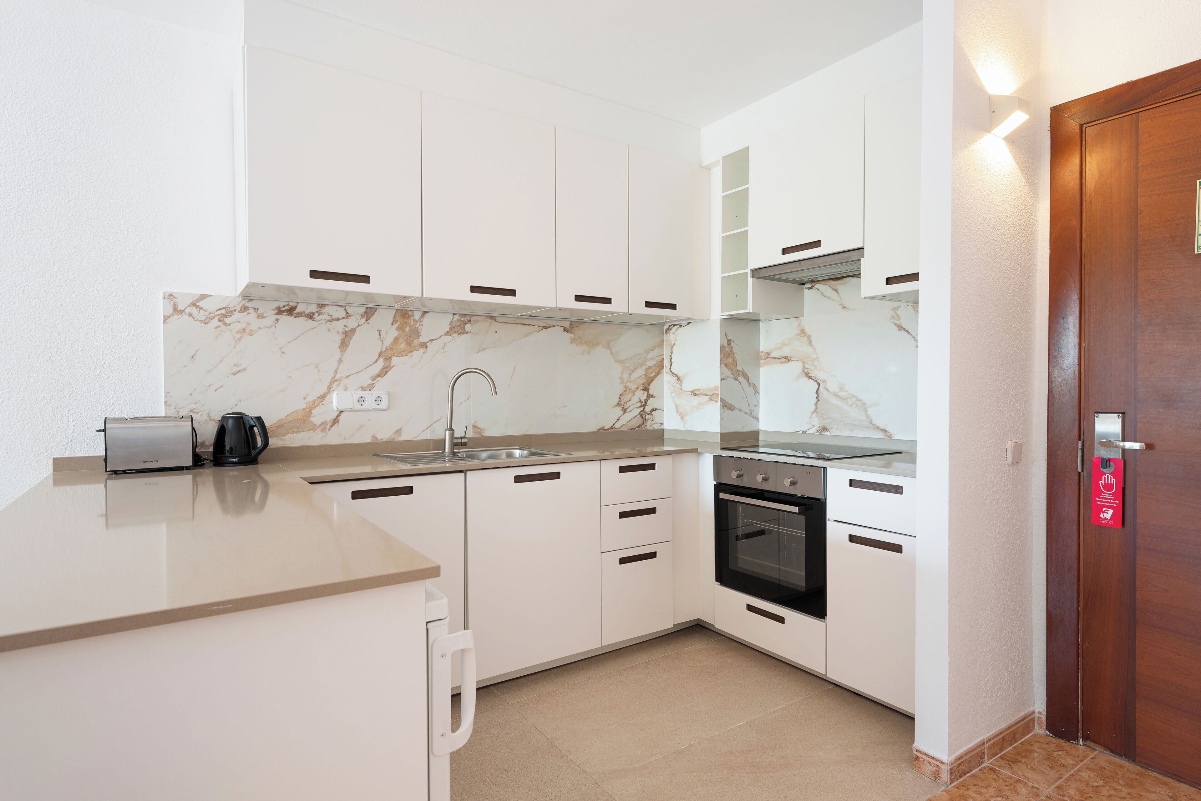 Una cocina moderna con armarios blancos, salpicadero de mármol, horno empotrado y cafetera.