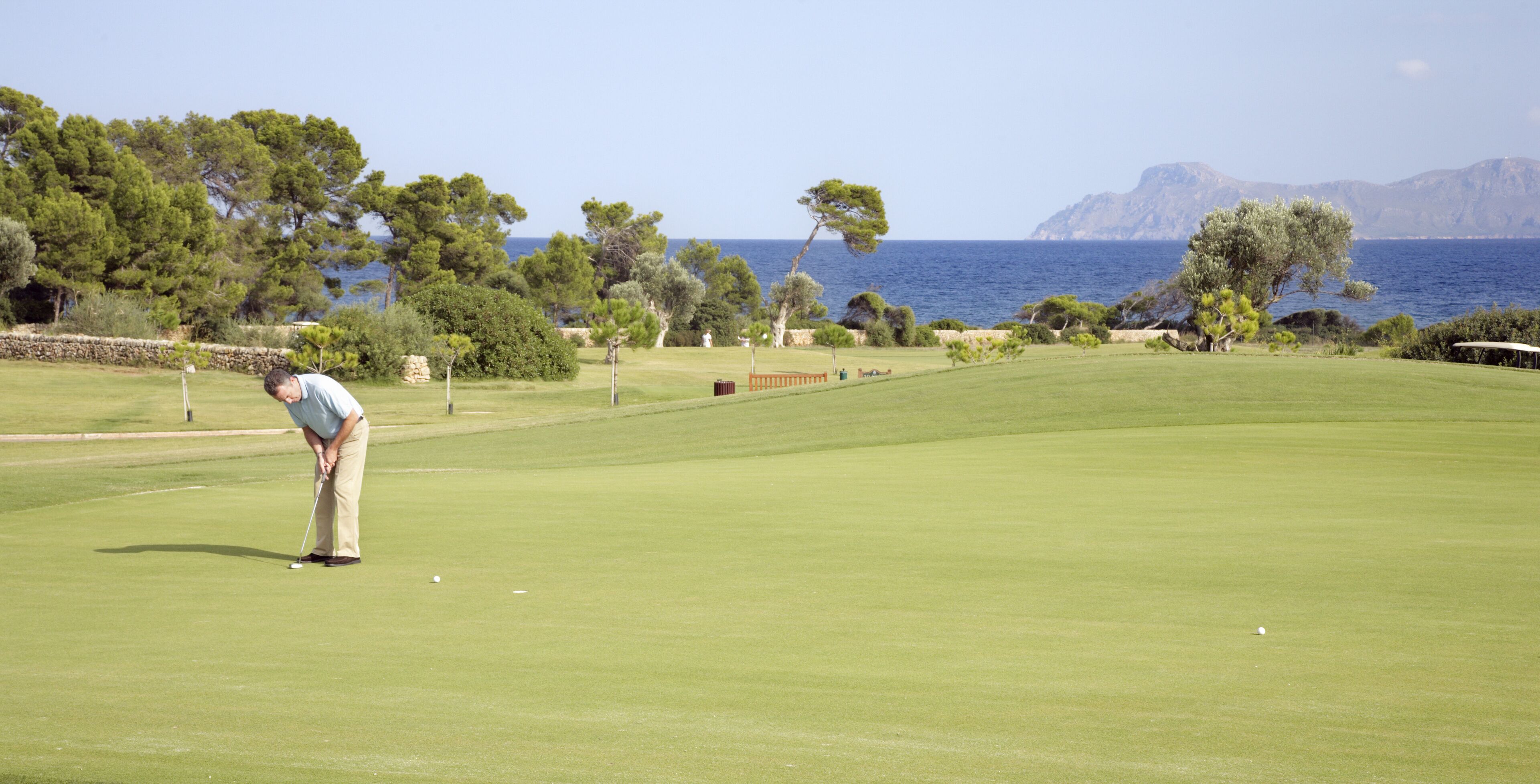 Een golfbaan met uitzicht op zee en bergen op de achtergrond.