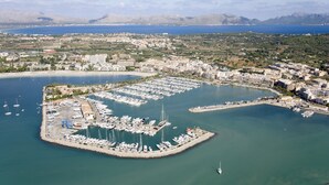 An aerial view of a marina with numerous boats docked, surrounded by residential buildings and a mountainous backdrop. - Apartamentos Siesta I (Alcúdia)