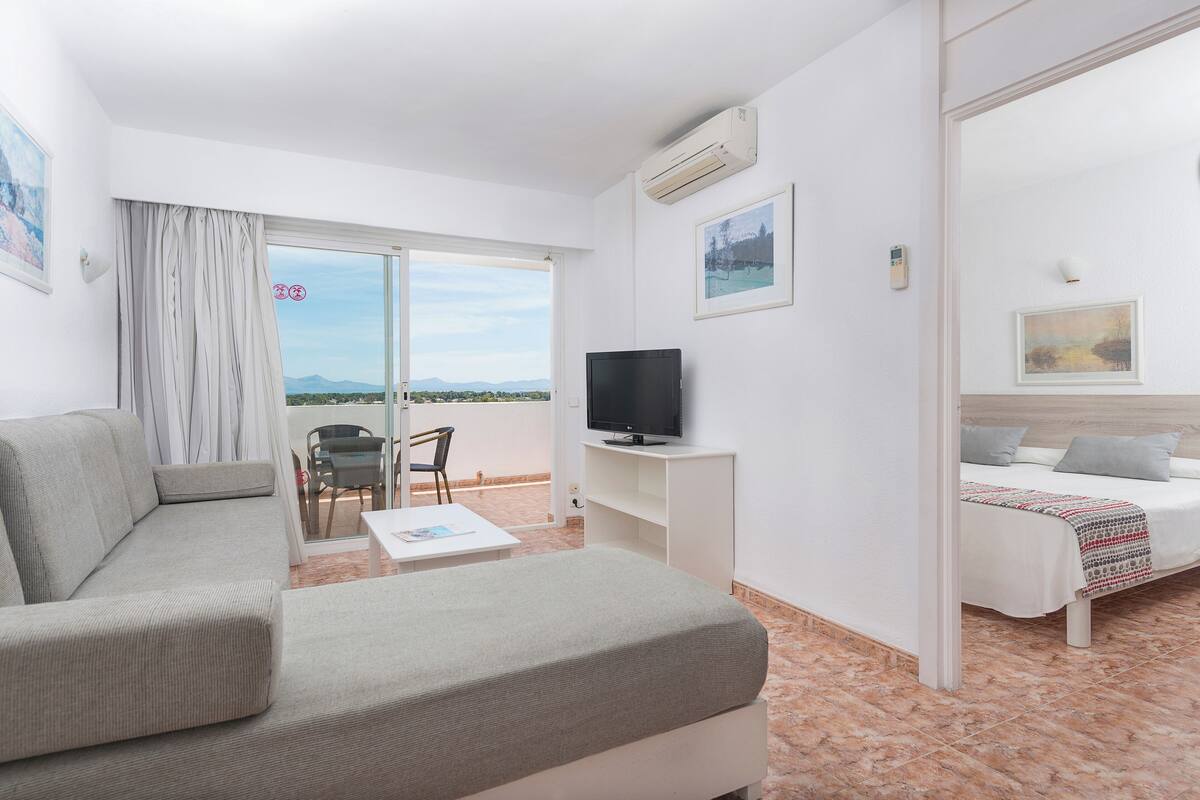 Ein Hotelzimmer mit Sofa, Fernseher, Bett, einem Balkon mit Blick und einem Esstisch.