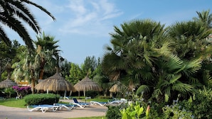 A resort with thatched umbrellas, palm trees, and lounge chairs. - Apartamentos Siesta I (Alcúdia)