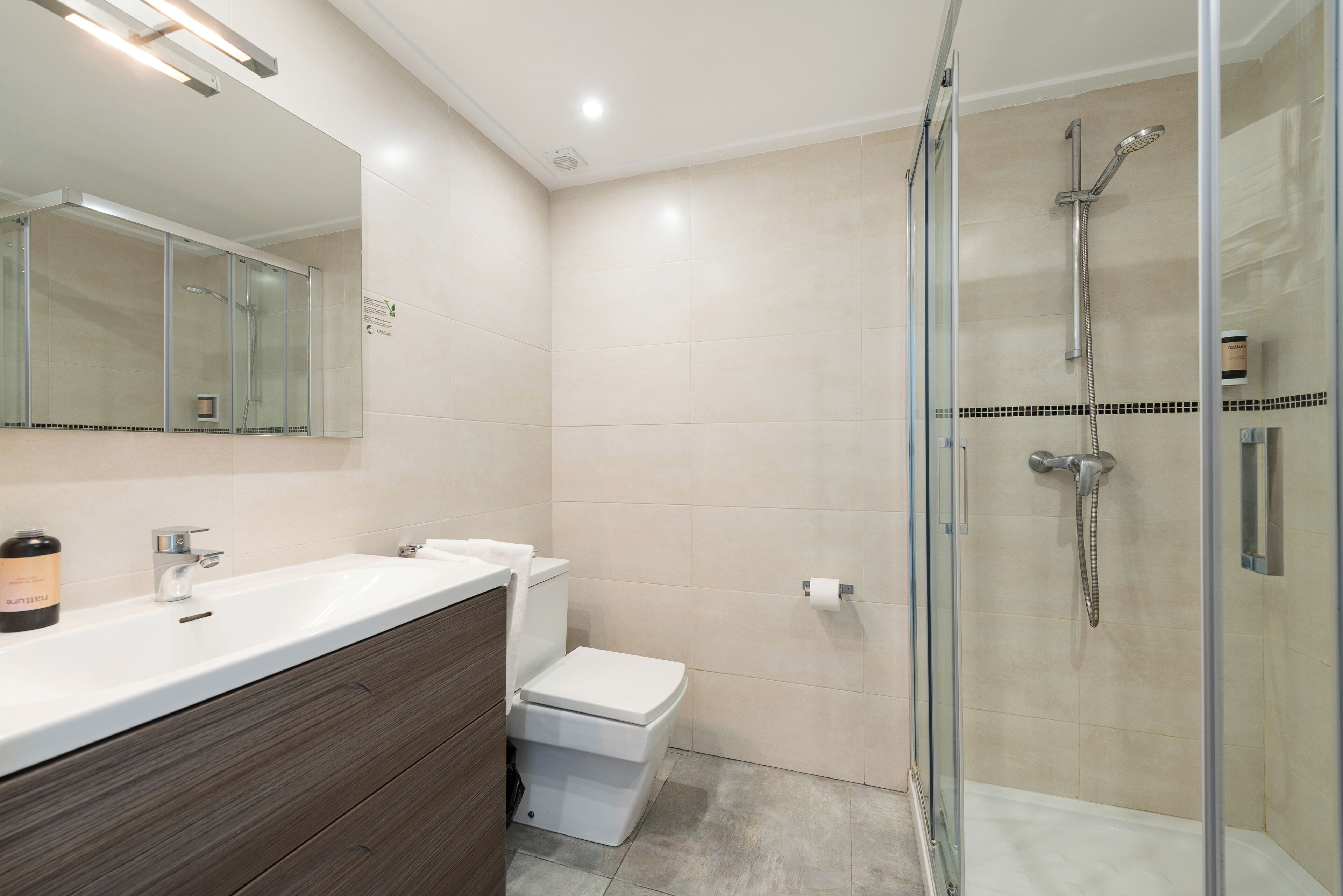 Une salle de bain moderne avec une douche à parois de verre, un lavabo blanc et un meuble-lavabo en bois.