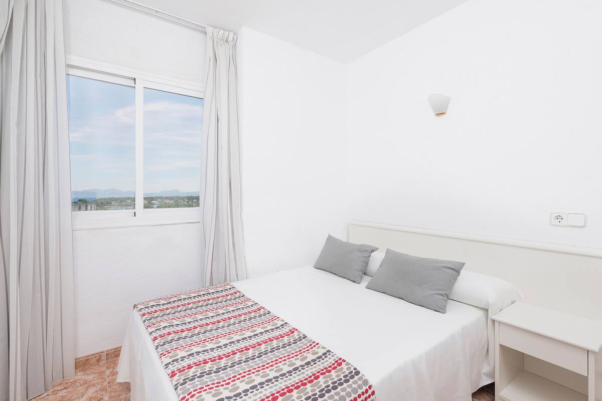 Ein Schlafzimmer mit Bett, Nachttisch, Fenster mit Vorhängen und Blick auf die Landschaft.