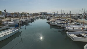 Uma marina com vários barcos atracados, um edifício ao fundo e água calma refletindo o céu.