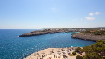 A coastal beach with clear blue waters, rocky formations, and a sandy area with umbrellas and lounge chairs.