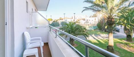 Un balcón con sillas de plástico blanco, barandilla metálica y vista a una zona residencial con palmeras y edificios.
