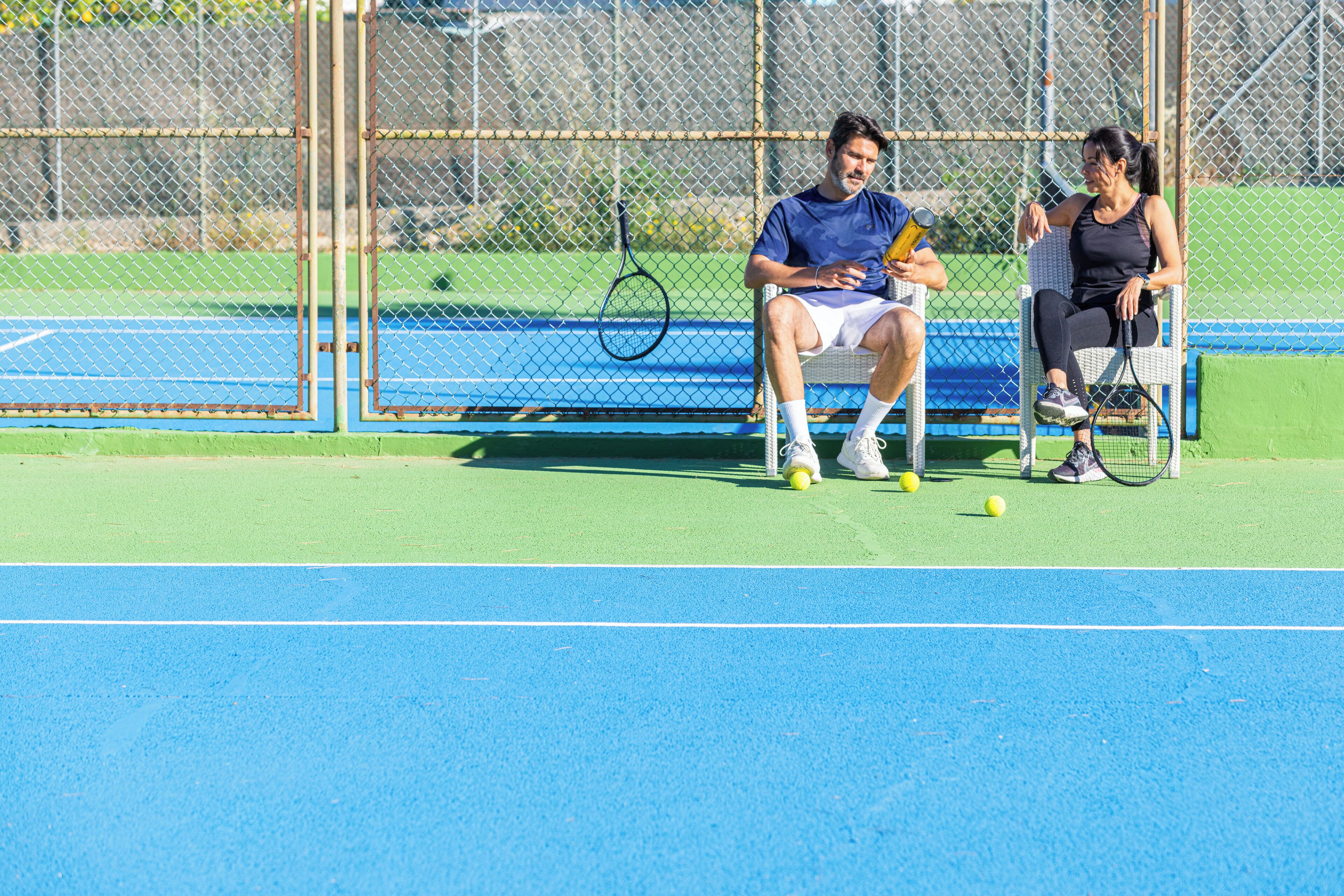 Un court de tennis avec un filet, un banc et des balles de tennis.