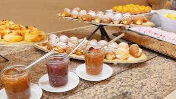 Un bufé con diversos pasteles y postres, incluyendo croissants y muffins, y dos frascos de mermelada.