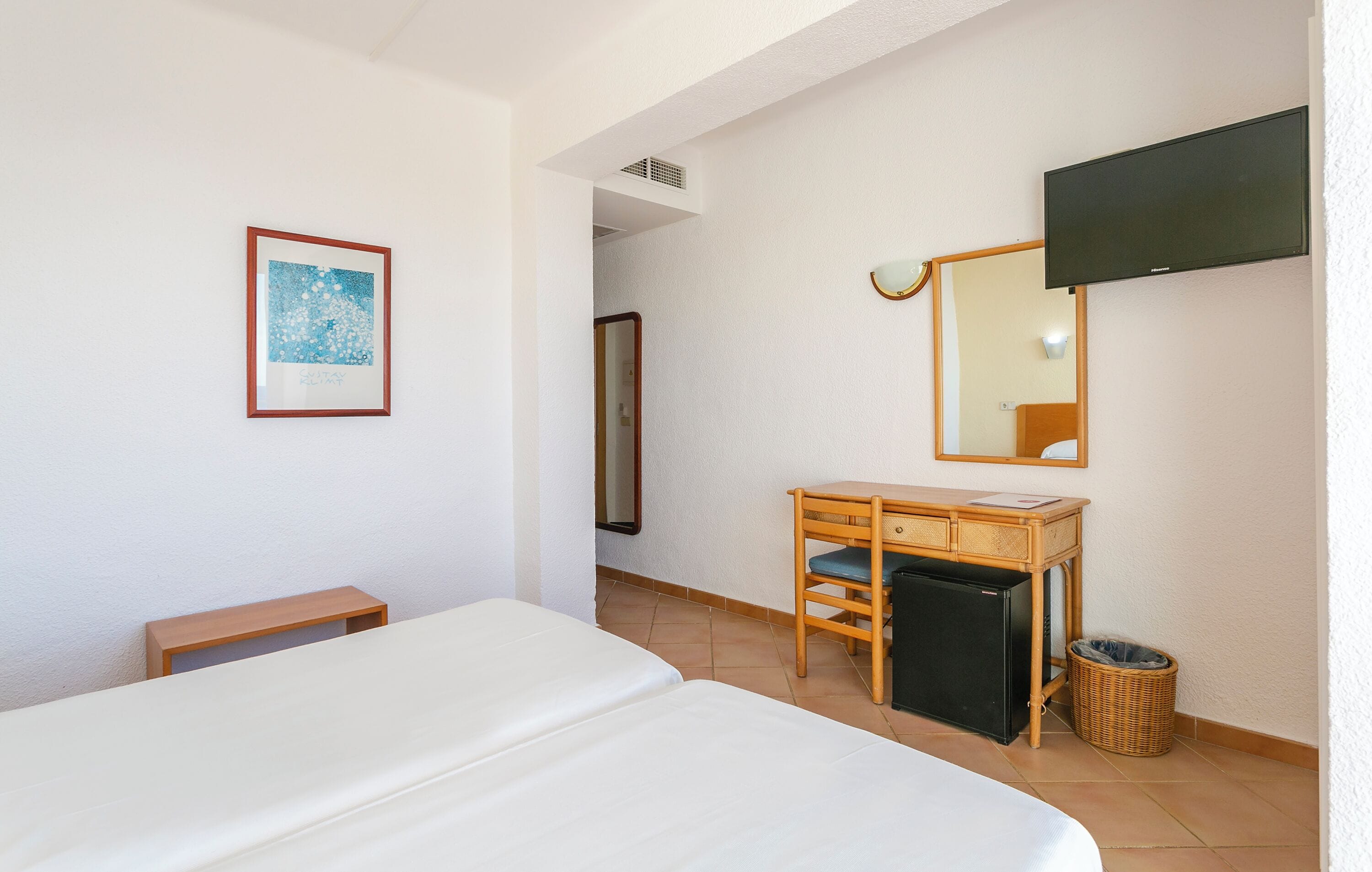 A hotel room with a bed, a wooden desk, a television, a framed picture, and a mirror.