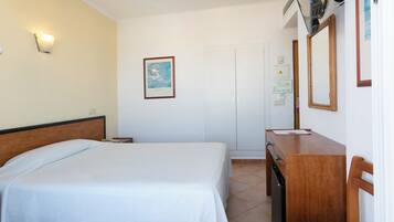 A hotel room with a bed, a desk, a chair, a mirror, and a wall-mounted light.