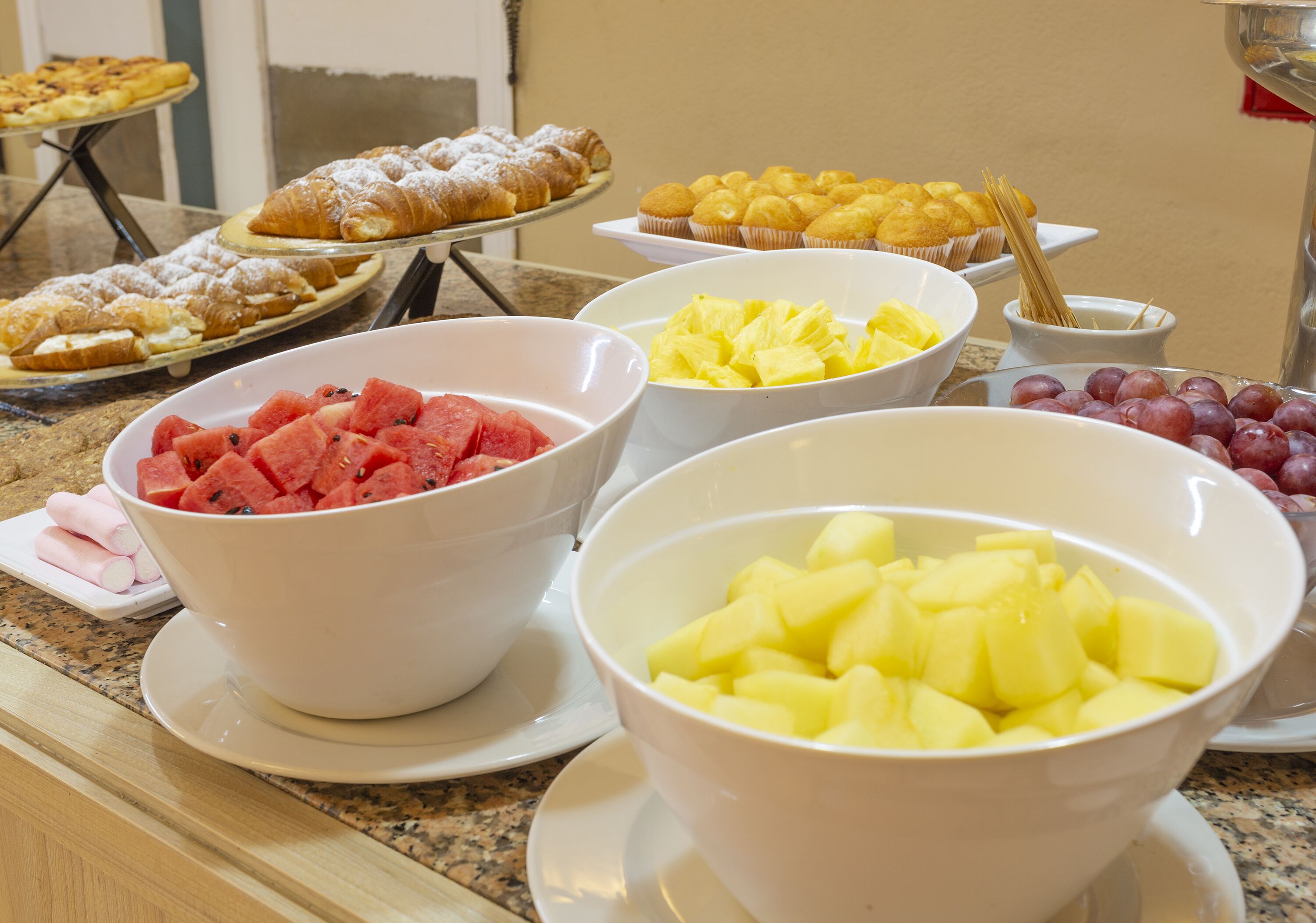 A buffet with various food items including watermelon, pineapple, grapes, and pastries.