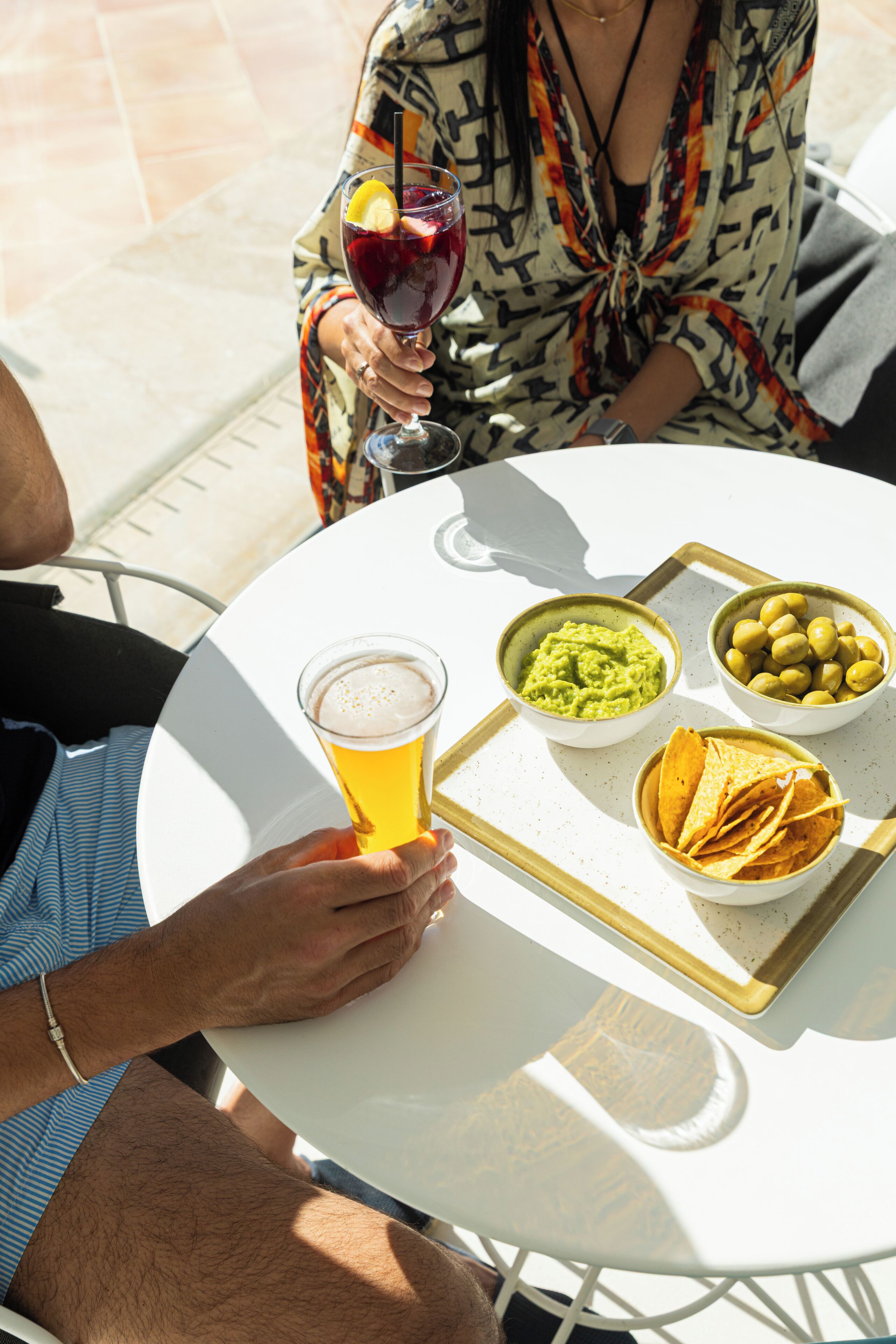 A round white table with a tray holding a glass of beer, bowls of guacamole and olives, and tortilla chips.