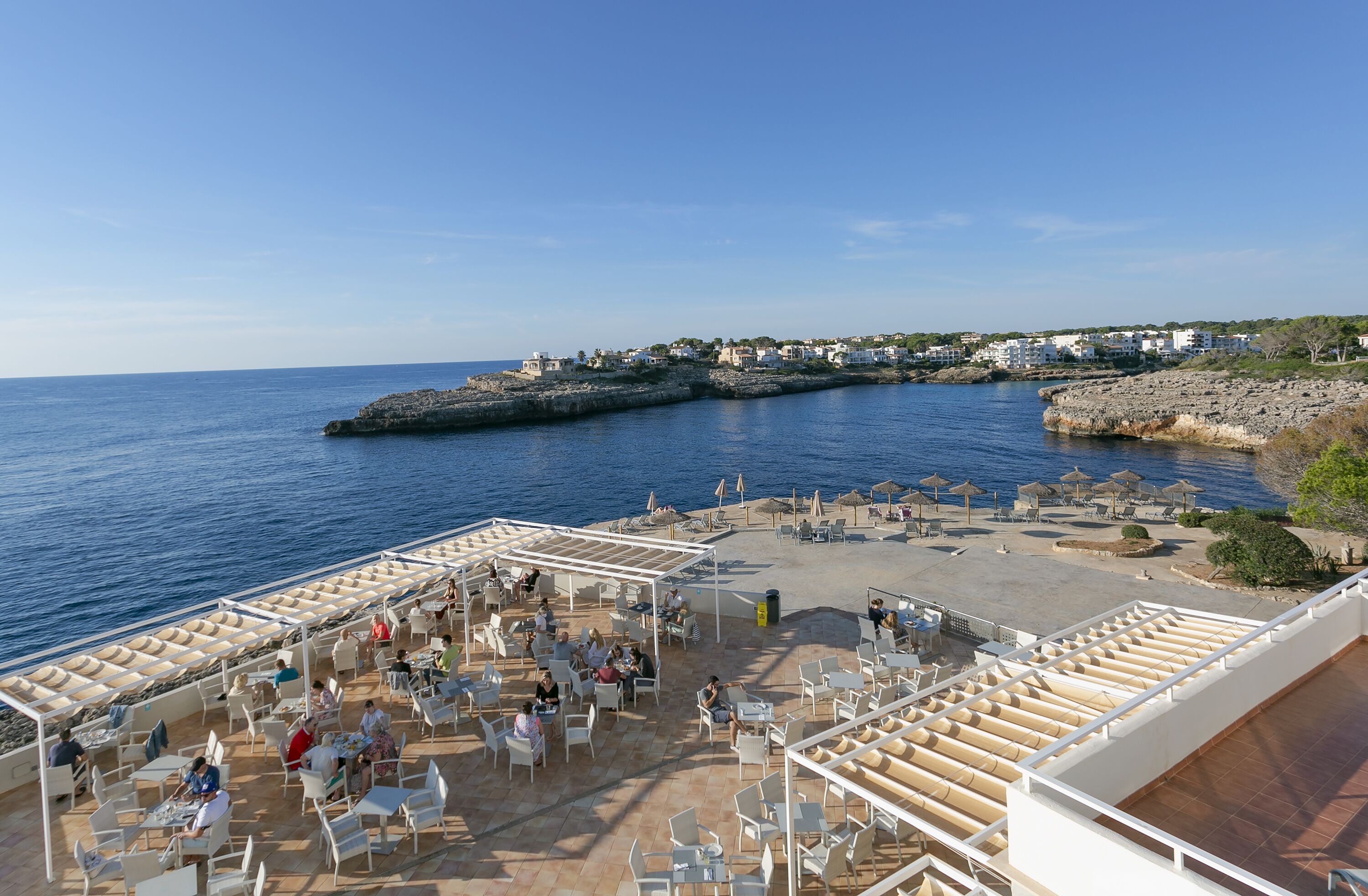 Una terraza costera con asientos al aire libre y vista al mar y edificios a lo lejos.