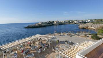 Una terraza costera con asientos al aire libre y vista al mar y edificios a lo lejos.